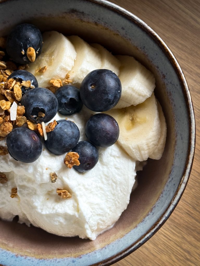 A close up photo from yoghurt with blueberries, granola, and banana. How to make homemade yoghurt by the A Hopeful Home blog.