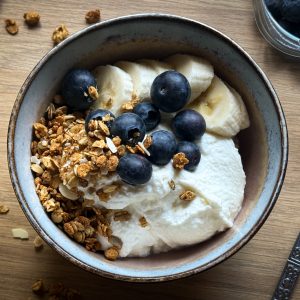 Header image how to make homemade yoghurt by the A Hopeful Home blog. The image shows a bowl of yoghurt with blueberries, granola, and banana on top.
